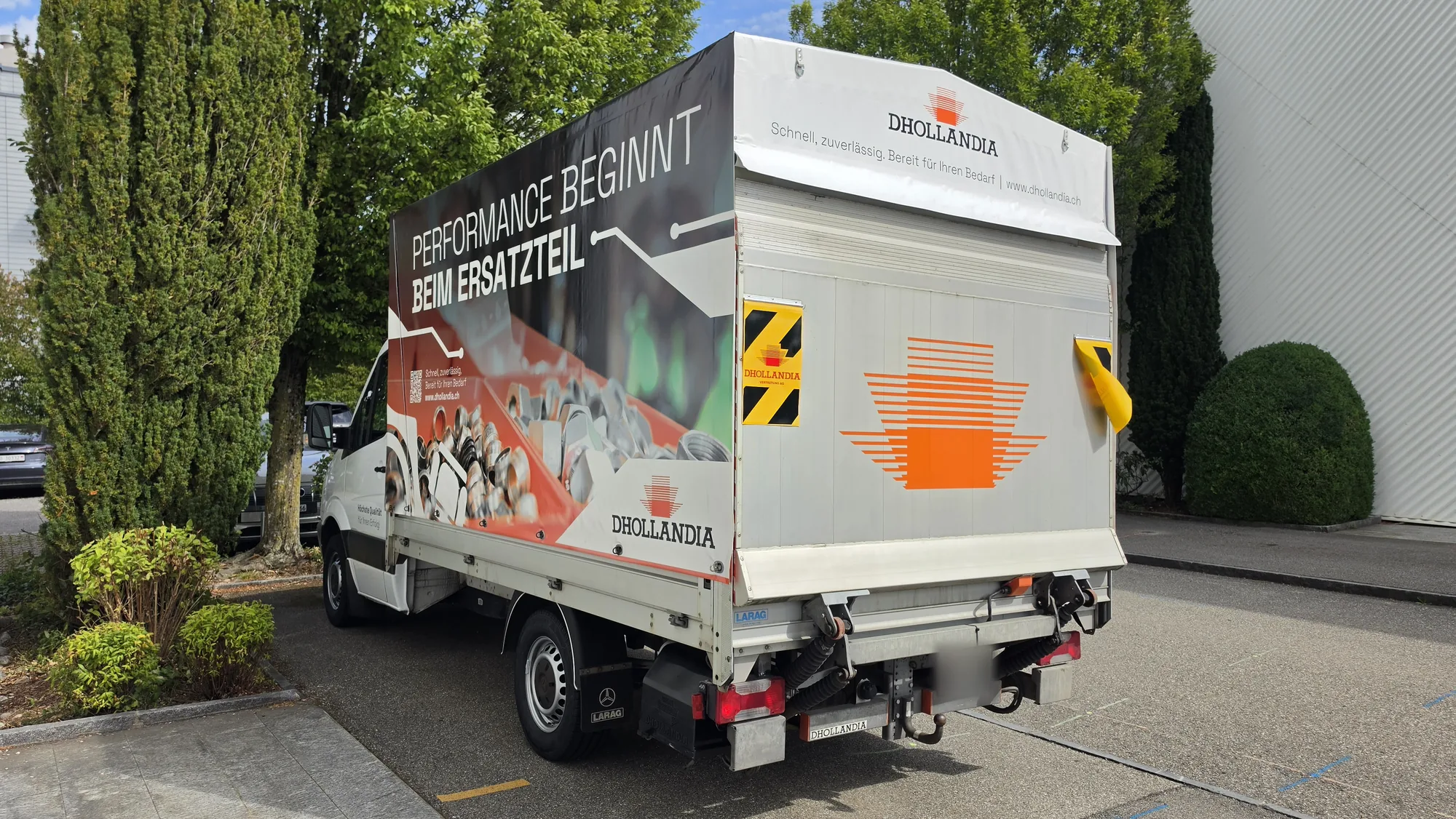 Heckansicht mit Blache «Performance beginnt beim Ersatzteil» und Dhollandia-Logo auf der Ladebordwand