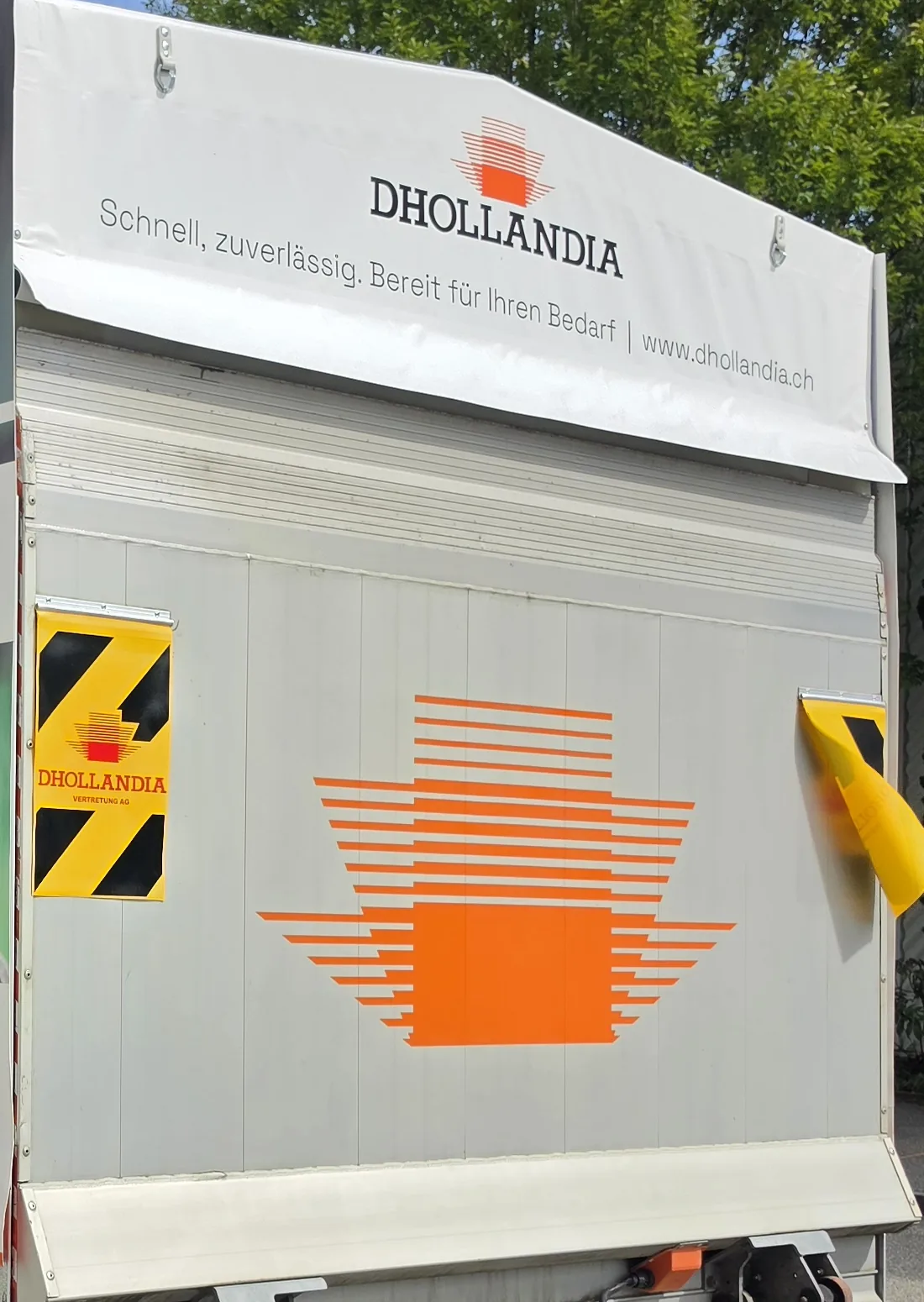Ladebordwand mit grossem Dhollandia-Logo aus orangem Plott und Slogan auf der Blache darüber